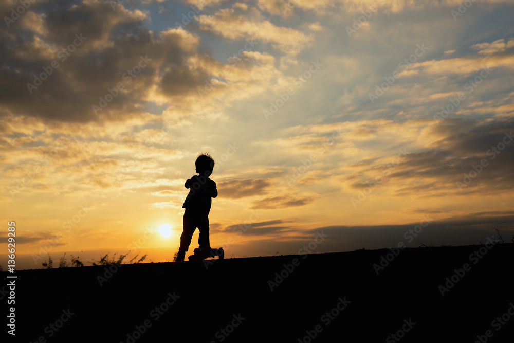 silhouette of a boy,little boy riding scooter at sunset time
