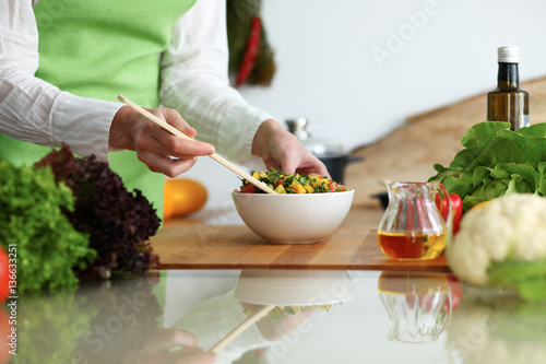 Closeup of human hands cooking vegetables salad in kitchen on the glass table with reflection. Healthy meal and vegetarian concept