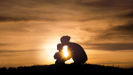 Silhouette of a young mother lovingly kissing her little child o