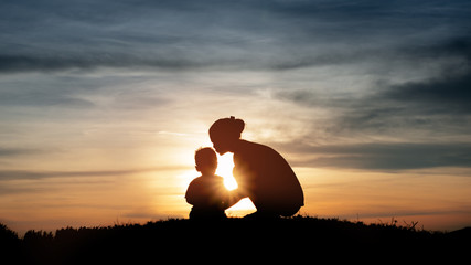 Silhouette of a young mother lovingly kissing her little child o