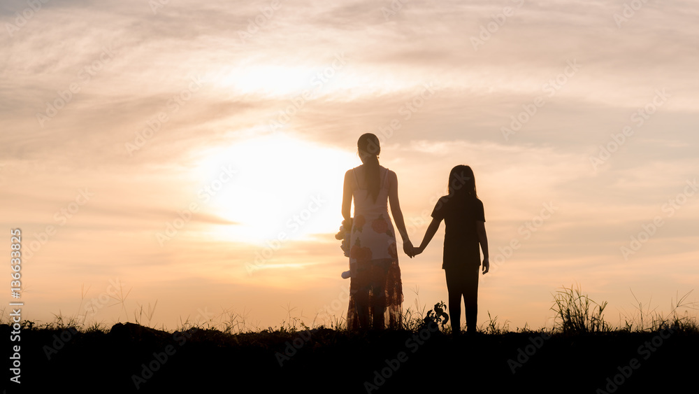 Silhouette of woman and her sister holding hands at sunset