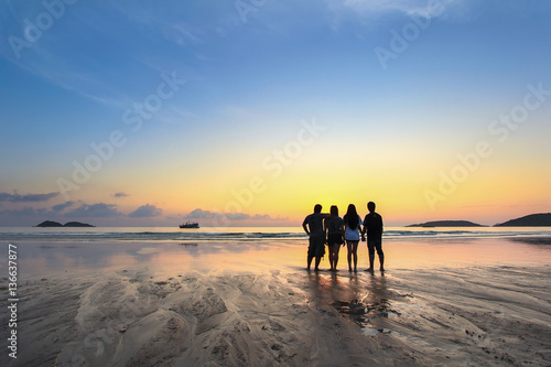 group of happy young people look on beautiful summer sunset at the beach