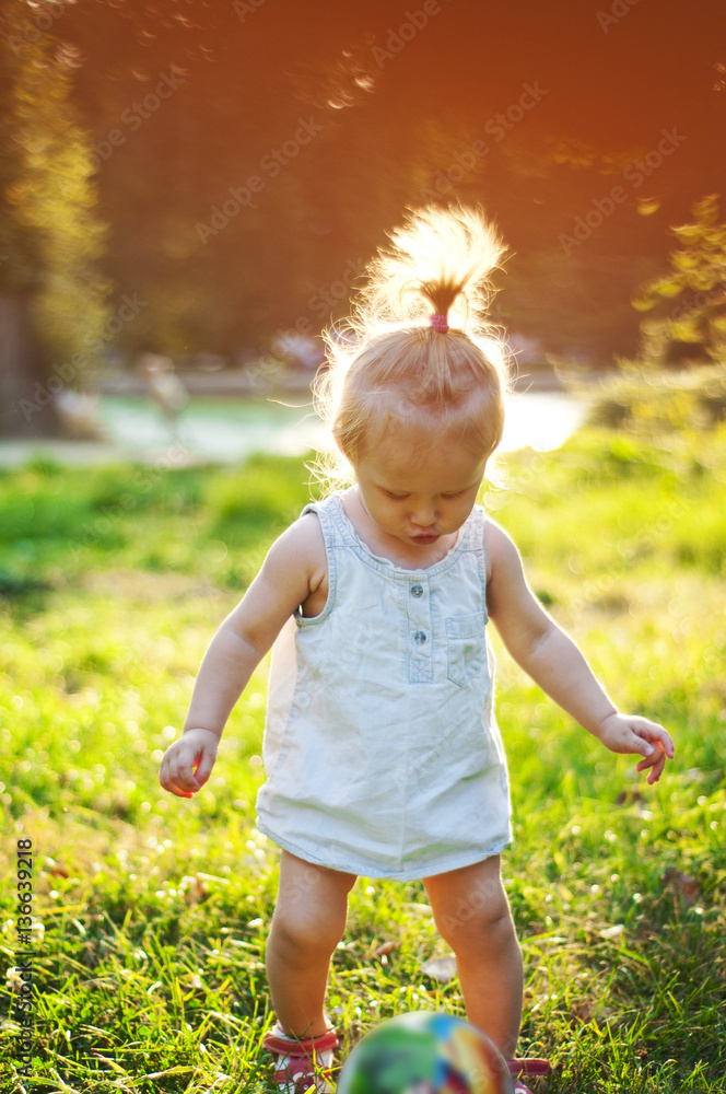 Cheerful little girl playing with a ball in a summer park at sun Cheerful little girl playing with a ball in a summer park at sun