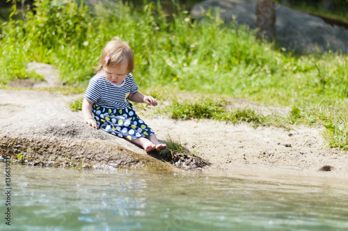 Fototapeta Naklejka Na Ścianę i Meble -  Little girl sitting on a river bank in the summer