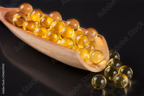 fish oil capsules in a wooden scoop on a dark background
