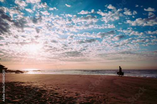 Bodyboarder walking across beach at sunrise