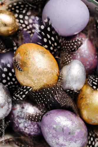 Violet, gold and silver easter eggs and beautiful decorative feathers close up