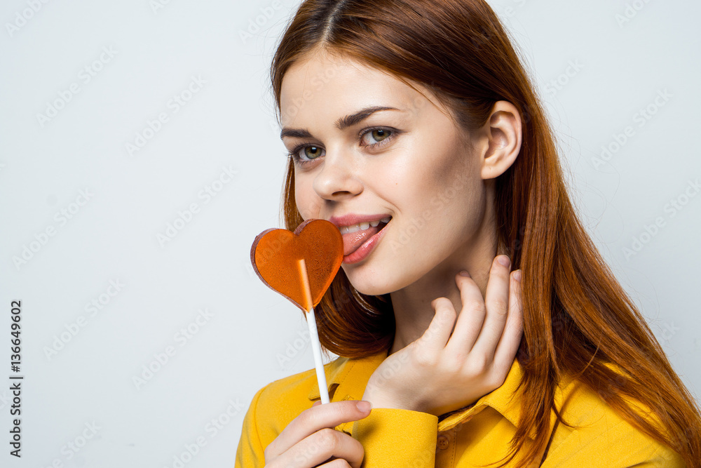 a woman licks a lollipop, a yellow shirt a woman licks a lollipop, a yellow shirt