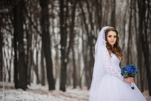 Pretty young bride with blue wedding bouquet at winter day on wo