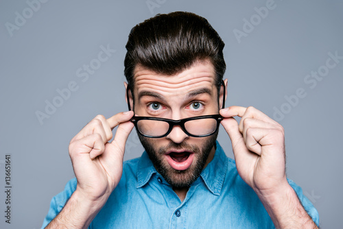 Wow  Surprised young man with opened mouth touching glasses