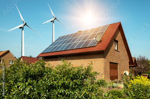 Solar panel on a roof of a house and wind turbins arround - concept of sustainable resources