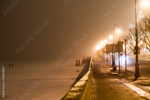 Palace Embankment in the fog on a winter night. Two people on the frozen Neva. © drbnth