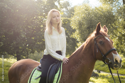 Молодая девушка со светлыми волосами сидит верхом на коричневой лошади в лесу  © natasidorova 