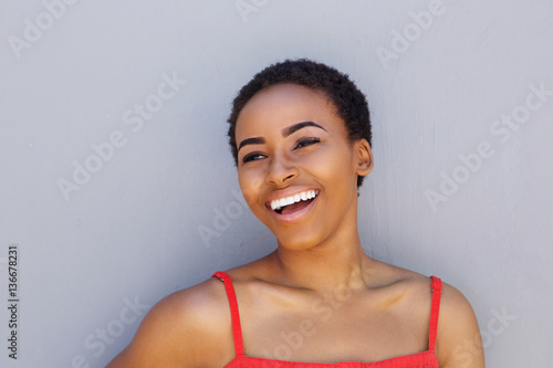 attractive young black woman laughing against gray wall