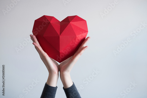 Fototapeta Two female hands holding red polygonal paper heart shape