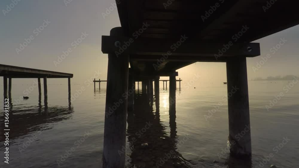 Walking under a wooden jetty at lake chiemsee, germany, bavaria against misty sky during dawn Walking under a wooden jetty at lake chiemsee, germany, bavaria against misty sky during dawn