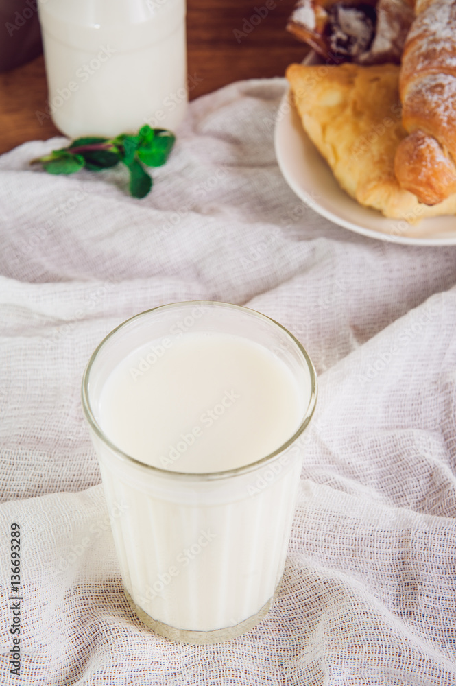 Glass of milk and plate with assortment of various fresh pastries and small bottle of milk on the background. Breakfast concept, selective focus Glass of milk and plate with assortment of various fresh pastries and small bottle of milk on the background. Breakfast concept, selective focus