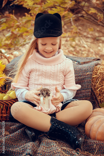 beautiful small girl with cute and funny hedgehog baby in autumn nature