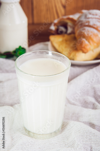 Glass of milk and plate with assortment of various fresh pastries and small bottle of milk on the background. Breakfast concept, selective focus