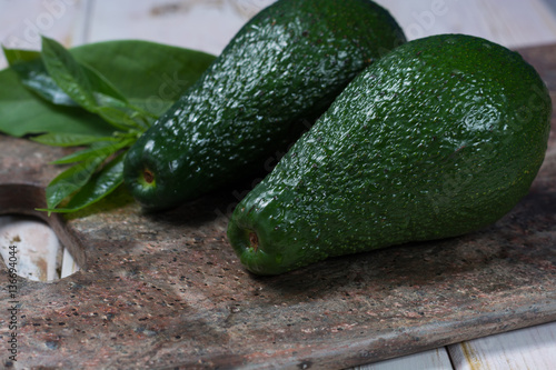 Green ripe avocado with leaves on granite plank