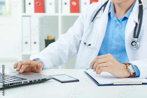 Young male medicine doctor sitting at the table and working at the laptop.