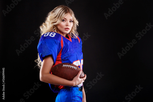 athletic blonde posing as american football girl on black background. Beautiful young woman wearing American football top holding ball. studio photo of american football woman