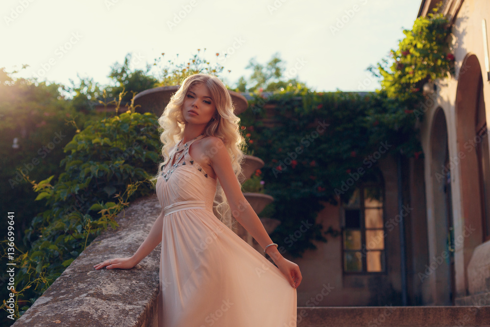 Young beautiful woman in long pink evening dress walking path in park. Fashion style portrait of gorgeous beautiful girl outdoors