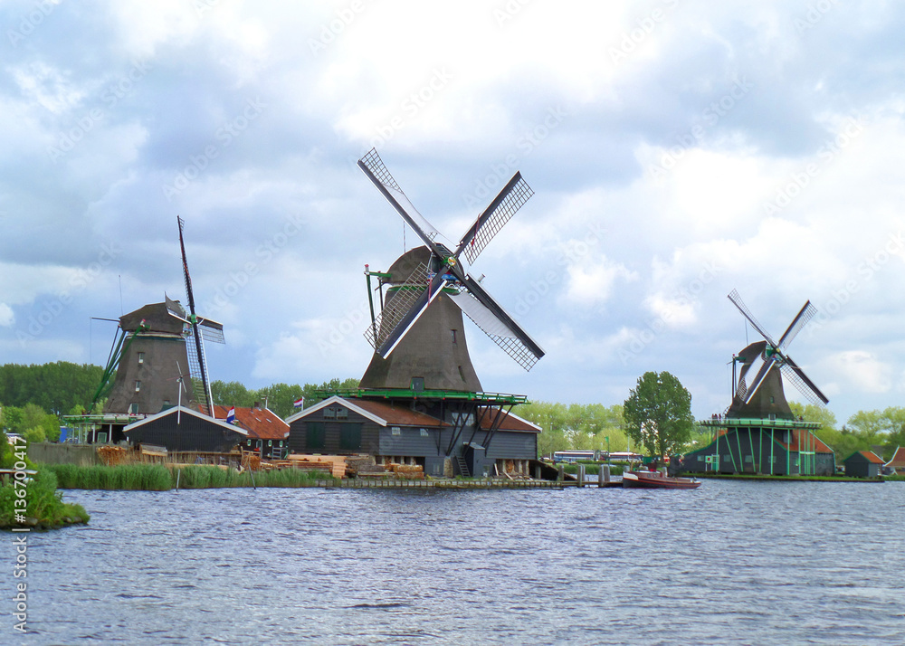 Three waterfront Dutch windmills against the cloudy sky, Zaanse Schans, Netherlands