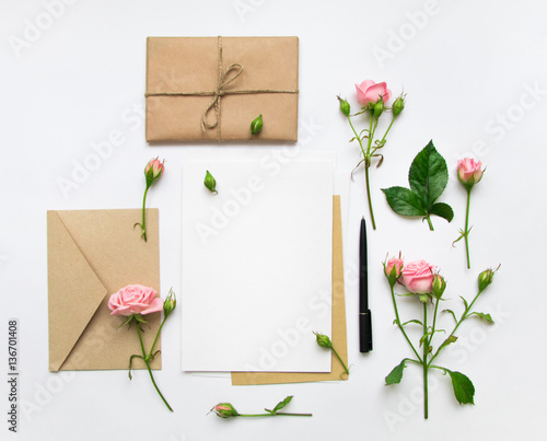 Letter, envelope and gift on white background. Invitation cards, or love letter with pink roses. Holiday concept, top view, flat lay