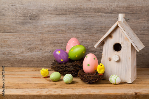 Easter holiday concept with eggs decoration, bird house and nest over wooden background