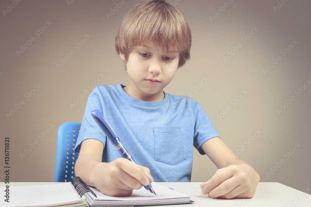 Boy using pen and writing on spiral paper notebook. Boy doing his homework exercises Boy using pen and writing on spiral paper notebook. Boy doing his homework exercises