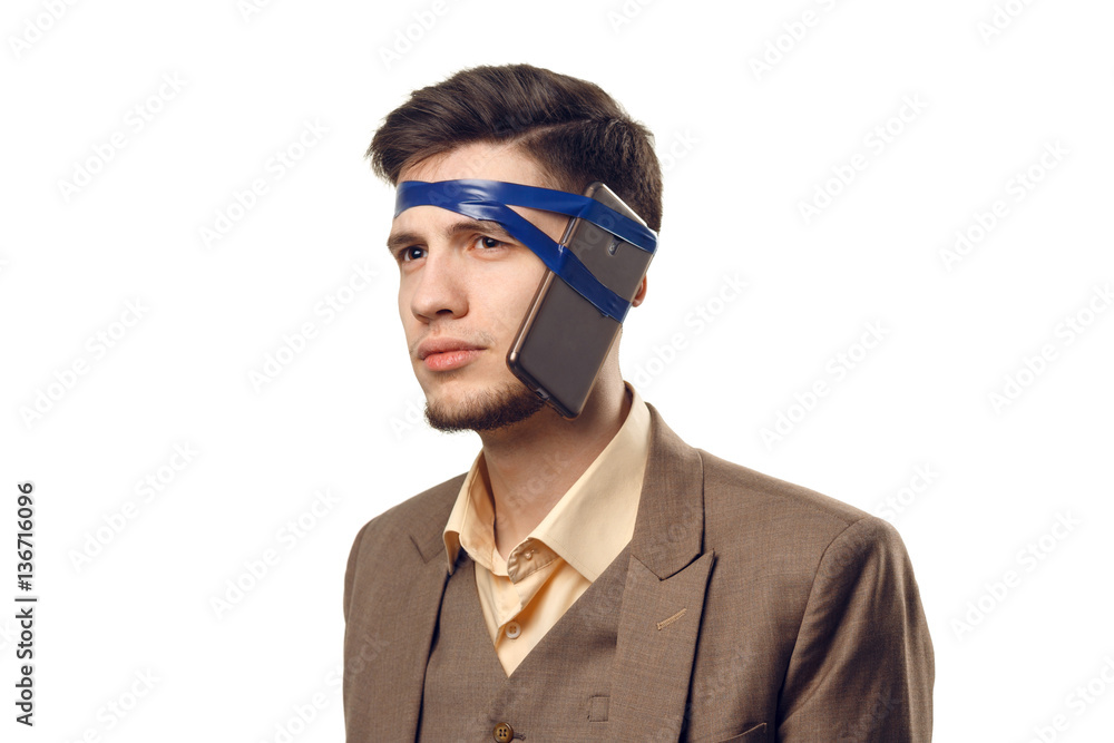 A humorous photo of modern technologies. Young guy with a phone attached to the head using a tape A humorous photo of modern technologies. Young guy with a phone attached to the head using a tape