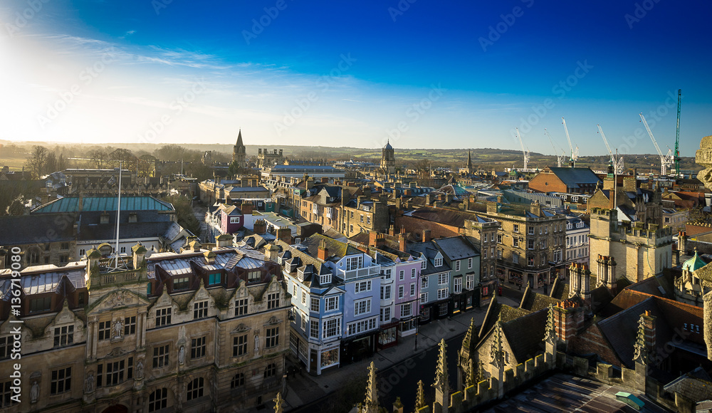 Aerial view of roofs and spires of Oxford, England with blue sky in background.