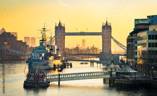 Fotografie HMS Belfast moored in front of Tower Bridge on the River Thames at sunrise