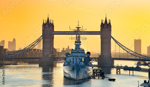 Fotografie HMS Belfast moored in front of Tower Bridge on the River Thames at sunrise
