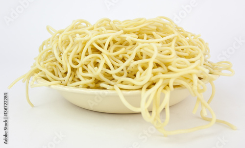 Spaghetti pasta with strands falling over edge of bowl. No sauce. White background.