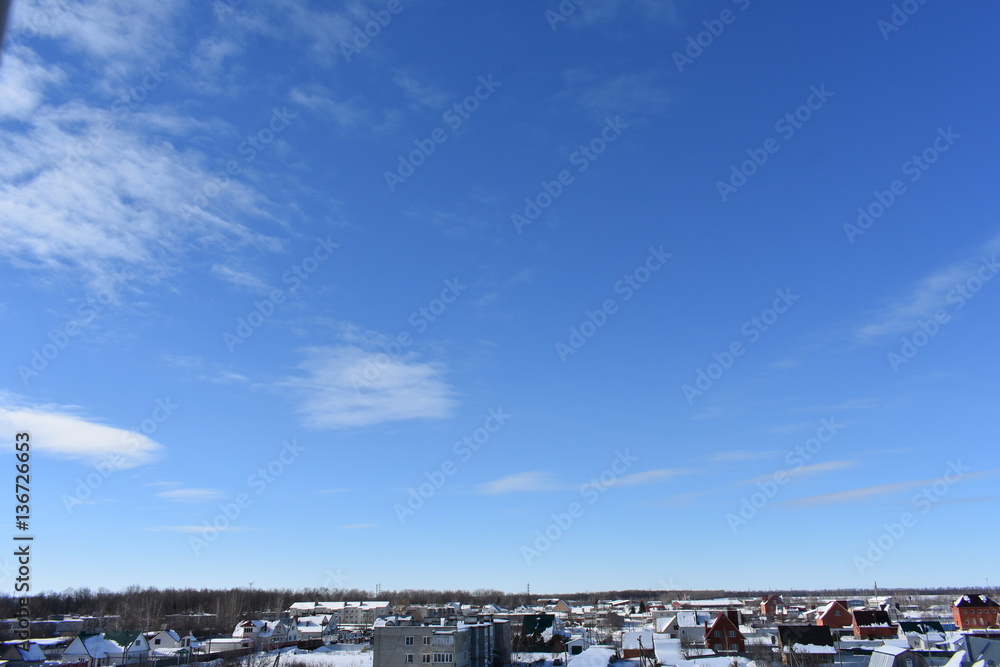 winter city on the background of blue sky; the house is covered with snow to the horizon; small clouds