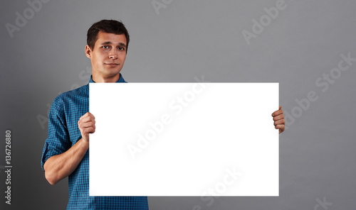 Pretty man holding empty white paper poster. Big billboard in hands of  handsome student. Studio portrait of person who keep blank board. Mockup  Stock Photo