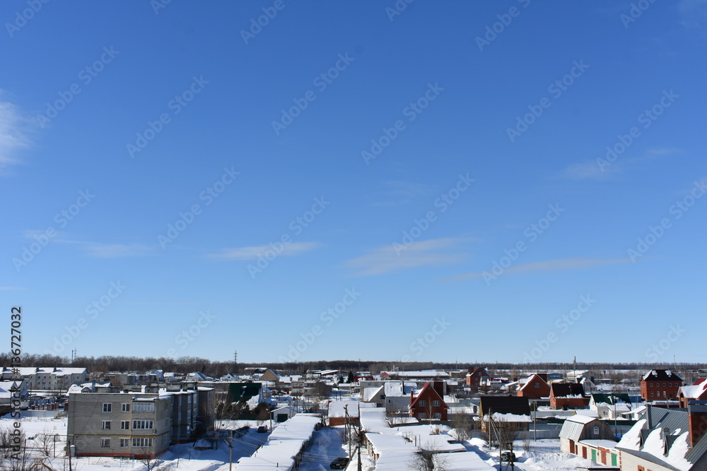 winter city on the background of blue sky; building house covered with snow to the horizon; small clouds