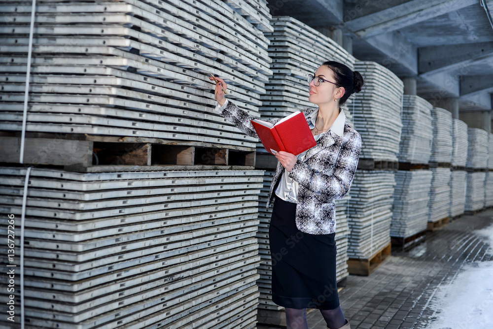 Φωτογραφία Girl storekeeper during operation recalculates the goods in the warehouse and is an accurate account of fixing all the goods in the red notebook