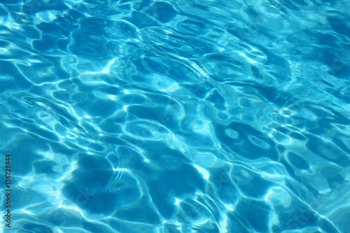 Blue water surface viewed from above in outdoor swimming pool, sun reflection, dimply.