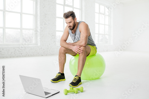 Man watching online trainig with laptop sitting on the fitball in the gym photo