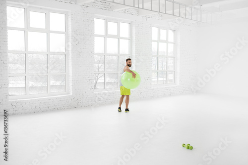 Wide shot of the white gym interior with big windows and man standing with fitball © rh2010