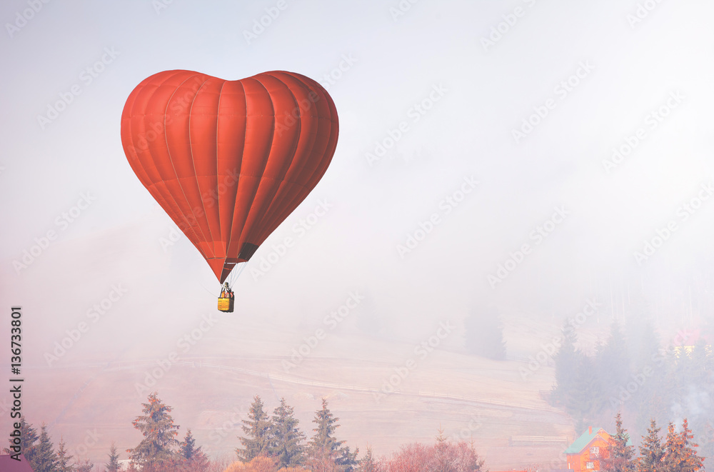 Obraz premium Red air balloon in shape of heart fly above forest in foggy morning. Romantic postcard background on Valentine's Day. Adventure trip for couples. Sport and recreation travel theme. Nature background
