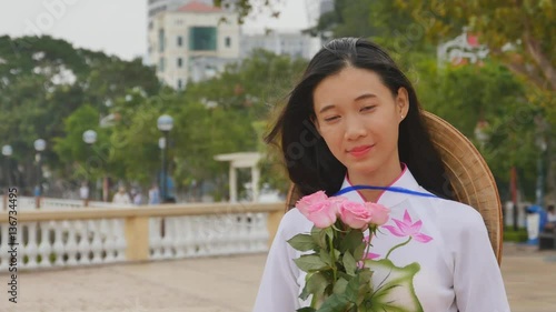 Vietnam girl in the national costume and dress Ao Dai posing and smiling for the camera. In the hands holding a pink rose. photo