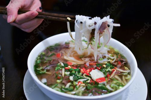 Girl eating traditional Vietnamese beef soup Pho Bo with chopsticks