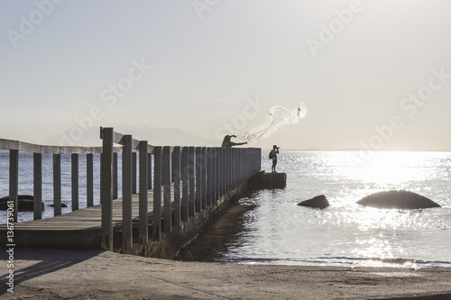Brazil, State of Rio de Janeiro, Paqueta Island, Man fishing and photographer on wooden dock during the sunset photo