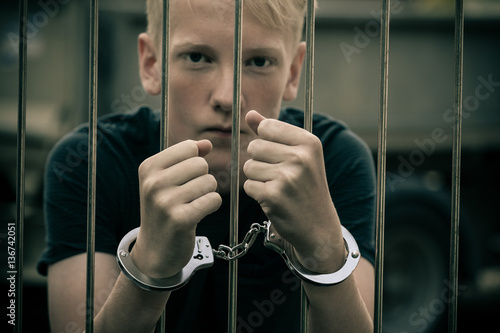 Murais de parede Handcuffed teenage boy behind bars