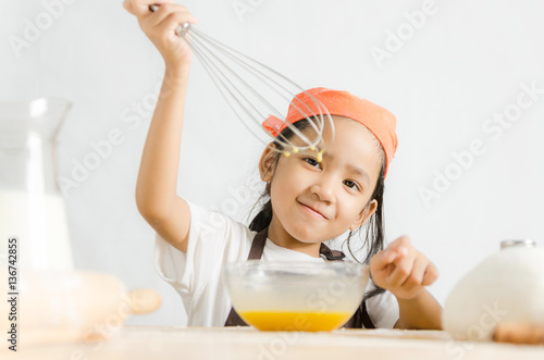 Asian little girl using stainless steel whisk to mix the egg for