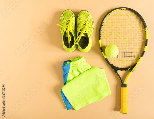 Tennis stuff on cream background. Sport, fitness, tennis, healthy lifestyle, sport stuff. Tennis racket, lime trainers, tennis balls, lime athletic shorts. Flat lay, top view.